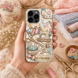 May include: A clear phone case featuring a collage of sewing supplies including a vintage sewing machine, scissors, spools of thread, a pincushion, and a measuring tape. The design includes a rectangular tag with the name Charlotte printed on it.