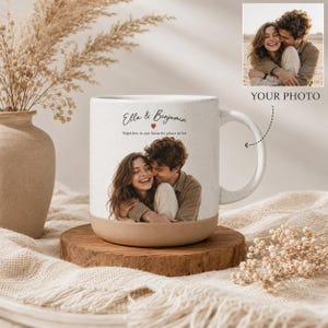May include: A white ceramic mug with a speckled finish and a tan base, featuring a custom photo of a couple, the names Ella & Benjamin, and the text Together is our favorite place to be with a small red heart icon printed on the front surface.