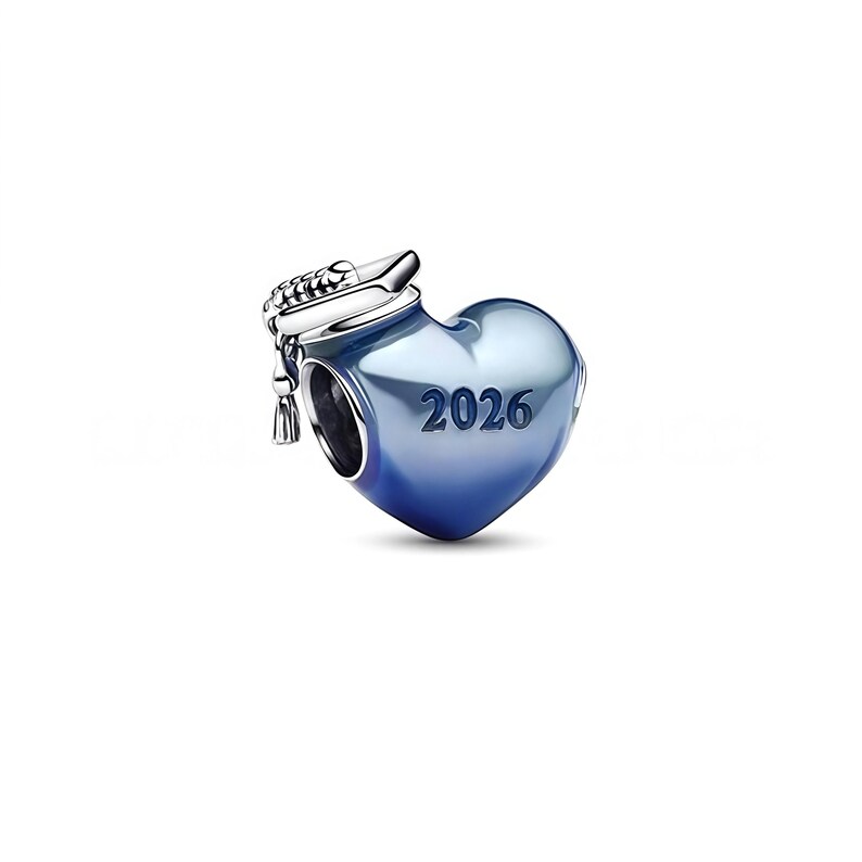 Może przedstawiać: Urok w kształcie serca z czapką absolwenta i rokiem "2026" wygrawerowanym na przodzie. Urok ma gradientowy niebieski kolor i srebrną czapkę absolwenta. Urok jest prawdopodobnie wykonany z metalu.
