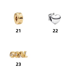 May include: Three jewelry charms labeled 21, 22, and 23. Number 21 is a gold-toned cylindrical charm with star engravings and small stones. Number 22 is a silver-toned heart charm with a graduation cap. Number 23 is a gold-toned charm spelling GOAL.