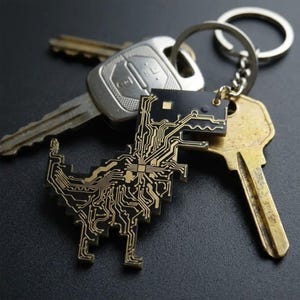 May include: A keychain featuring a black dinosaur-shaped circuit board with gold-colored conductive traces, attached to a silver-toned metal split ring along with two standard metal house keys. The dinosaur design has a pixelated appearance.