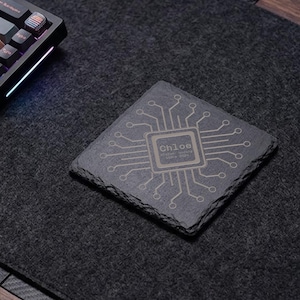 Peut inclure: Un dessous de verre carré en ardoise gris foncé avec un bord naturel et rugueux. La surface présente un motif de circuit imprimé gravé au laser centré autour d'un design de puce rectangulaire contenant le nom Chloe et du texte.
