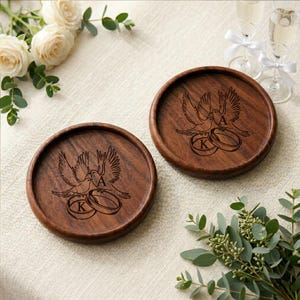 May include: Two round dark brown wooden coasters featuring a laser-engraved design of two birds perched above two interlocking rings. The letter K is engraved on one ring and the letter A is engraved on the other ring within the circular wood grain.