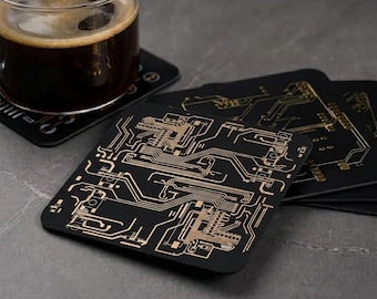 May include: Black square coasters with a gold circuit board design. One coaster holds a glass of dark liquid. The coasters are made of a durable material and are suitable for use with hot or cold beverages.