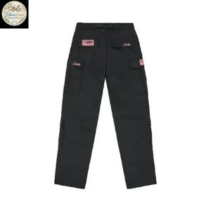 May include: Black cargo pants with multiple pockets and a belt loop. The pants have pink rectangular patches with text and pink script on the pockets. The pants are displayed on a white background.