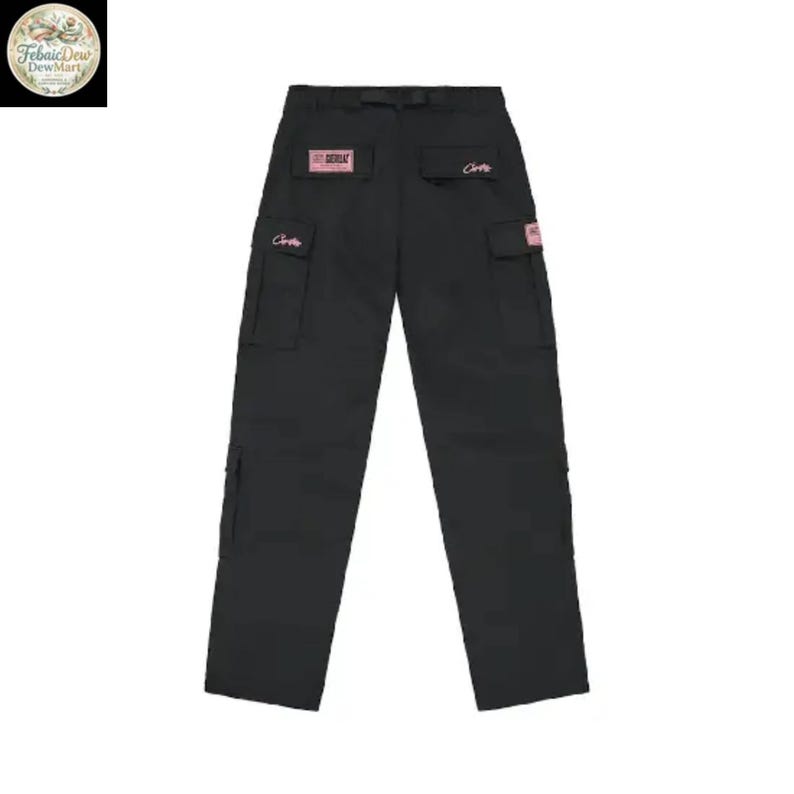 May include: Black cargo pants with multiple pockets and a belt loop. The pants have pink rectangular patches with text and pink script on the pockets. The pants are displayed on a white background.
