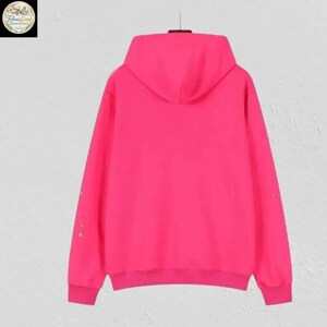 May include: A vibrant pink hoodie with a hood and long sleeves. The hoodie has a ribbed hem and cuffs. Small, colorful floral accents are visible on the left sleeve. The hoodie is displayed against a plain background.
