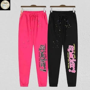 May include: Two pairs of sweatpants, one hot pink and one black, each with a drawstring waist. The hot pink pants have the word "Spidey!" in a sparkly design on the left leg. The black pants have the same design in a neon color.