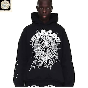 Pode incluir: Moletom preto com estampa de teia de aranha branca e o texto "sp5der". O moletom tem mangas compridas e capuz com cord&atilde;o. A manga esquerda tem detalhes de estrelas brancas.