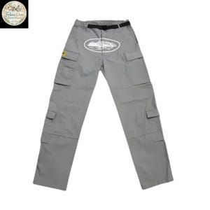 May include: Gray cargo pants with multiple pockets and a black belt. An oval graphic with a white illustration of a building is centered on the front. A small yellow patch is on the left pocket.
