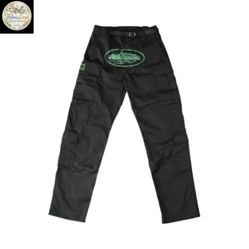 May include: Black cargo pants with multiple pockets and a belt. A green oval design with a landscape is centered on the front. The pants have a small green square patch on the left pocket. The pants are made of a durable material.