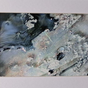 Op de afbeelding: Abstracte kunstafdruk met een mix van blauwe, witte en zwarte tinten. Het kunstwerk heeft een textuur met organische vormen en patronen. De afdruk is gemonteerd in een witte passe-partout.