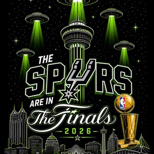 May include: A black graphic print featuring the San Antonio skyline with the Tower of the Americas, UFOs emitting green light beams, the text THE SPURS ARE IN THE FINALS 2026, and a gold NBA championship trophy on a dark starry background.