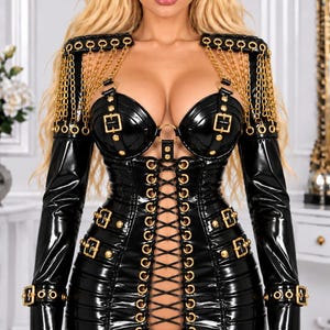 May include: A black patent leather mini dress featuring long sleeves, gold-tone chain shoulder accents, and gold-tone buckles. The bodice includes moulded cups, while the front centre features a vertical lace-up closure with gold-tone grommets.