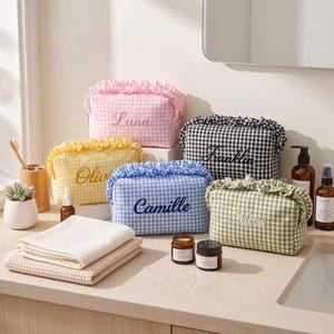 May include: Five rectangular toiletry bags with ruffled tops and gingham patterns in pink, yellow, blue, black, and green. Each bag features a personalised name embroidered on the front: Luna, Olivia, Camille, Franklin, and Moss.