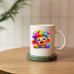 May include: A white ceramic mug featuring a colorful graphic of a cartoon monkey with bright rainbow-colored fur, large blue eyes, and a wide smile. The monkey character is depicted with swirling patterns in its hair and ears, set against a plain white background.