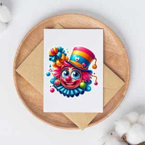 May include: A white greeting card featuring a colorful illustration of a clown face with bright pink hair, a blue ruffled collar, and a striped top hat adorned with a small white heart. The clown has large blue eyes and a red nose.