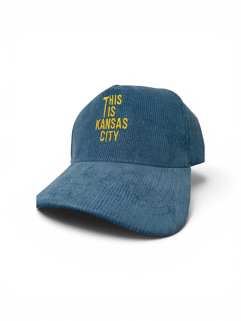 May include: A blue corduroy baseball cap with the text "THIS IS KANSAS CITY" embroidered in yellow. The cap has a curved brim and a structured crown, suitable for casual wear.