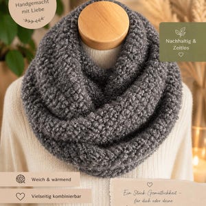 Könnte beinhalten: Grauer, grob gestrickter Loop-Schal auf einem hölzernen Mannequinkopf. Der Schal ist aus weichem, strukturiertem Garn gefertigt und wird um den Hals getragen. Der Schal hat eine neutrale Farbe und passt zu vielen Outfits.