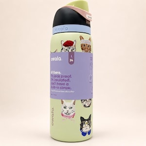 May include: A light green Owala water bottle with a black and light blue lid, featuring a wrap-around purple label with cat illustrations and text that reads: Hi there. I'm leak proof. I'm insulated. And I have a built-in straw. 24 oz (710 ml).