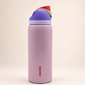 Pu&ograve; includere: Una borraccia cilindrica color viola chiaro con finitura opaca. La borraccia presenta un tappo multicolore nelle tonalit&agrave; viola, rosso e beige. Il marchio Owala &egrave; stampato in rosso sulla parte inferiore e in bianco sul colletto del tappo.
