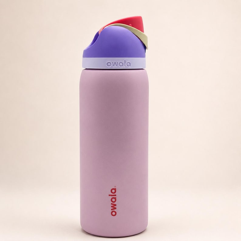 Pu&ograve; includere: Una borraccia cilindrica color viola chiaro con finitura opaca. La borraccia presenta un tappo multicolore nelle tonalit&agrave; viola, rosso e beige. Il marchio Owala &egrave; stampato in rosso sulla parte inferiore e in bianco sul colletto del tappo.