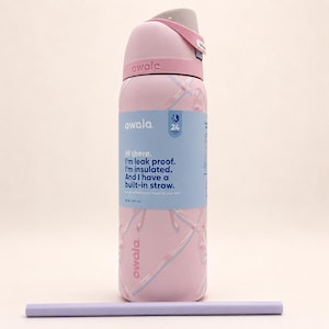May include: A light pink Owala insulated water bottle with a 32 oz capacity, featuring a gray lid, a built-in straw, and a blue label with the text: Hi there. I'm leak proof. I'm insulated. And I have a built-in straw. A separate light purple straw lies below.