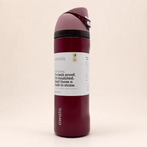 May include: A dark red Owala water bottle with a mauve lid and a built-in straw. The bottle features a white label with the text: Hi there. I'm leak proof. I'm insulated. And I have a built-in straw. The label also indicates a 24-ounce capacity.