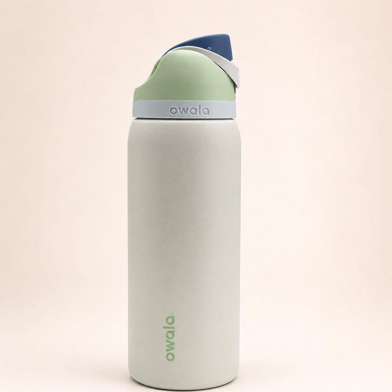 Pu&ograve; includere: Una borraccia Owala grigio chiaro con un coperchio verde pallido e blu scuro. La bottiglia presenta un corpo cilindrico con il nome del marchio Owala stampato in verde vicino alla base e in rilievo bianco sulla parte grigia del coperchio.