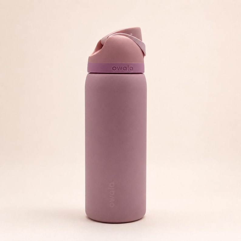 Pu&ograve; includere: Una borraccia cilindrica Owala in una tonalit&agrave; malva tenue. La bottiglia presenta una finitura opaca con un coperchio malva pi&ugrave; scuro e un manico integrato rosa chiaro. Il marchio Owala &egrave; impresso sul coperchio e stampato sul corpo della bottiglia.