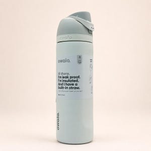 May include: A light blue Owala insulated water bottle with a gray lid and a built-in straw. The bottle features a white label with the text: Hi there. I'm leak proof. I'm insulated. And I have a built-in straw. It has a 24 oz capacity.