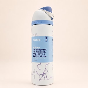 May include: A white Owala water bottle with a blue lid and a light blue wrap featuring the text: Hi there. I'm leak proof. I'm insulated. And I have a built-in straw. 24 oz. (710 ml). The bottle body has a light purple ribbon pattern printed on it.