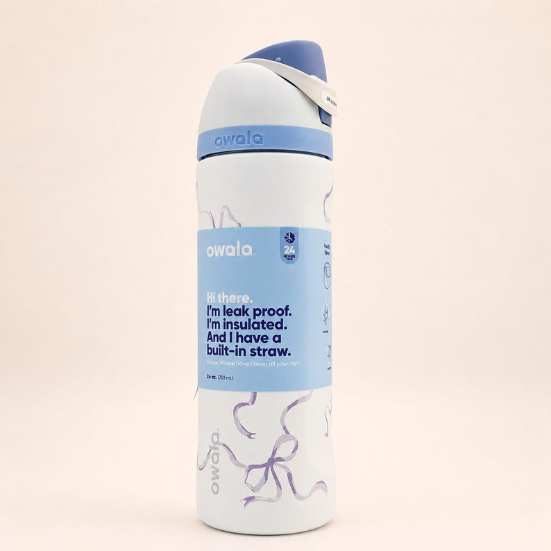 May include: A white Owala water bottle with a blue lid and a light blue wrap featuring the text: Hi there. I'm leak proof. I'm insulated. And I have a built-in straw. 24 oz. (710 ml). The bottle body has a light purple ribbon pattern printed on it.