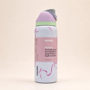Pu&ograve; includere: Una borraccia Owala bianca con capacit&agrave; di 946 ml, dotata di coperchio viola chiaro e verde, manico grigio e grafiche a nastro rosa. Un'etichetta riporta: Hi there. I'm leak proof. I'm insulated. And I have a built-in straw. 32 oz. (946 mL).
