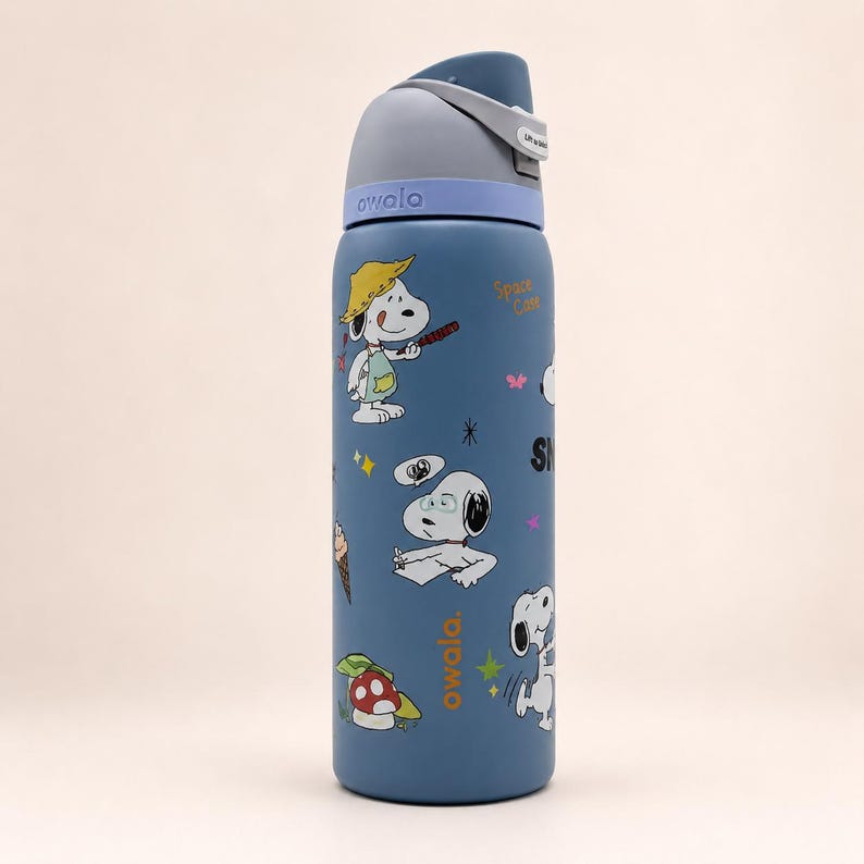 May include: A blue Owala water bottle featuring Snoopy graphics, including Snoopy wearing a yellow hat, writing at a desk, and holding an ice cream cone. The bottle has a gray and light blue lid with a carry loop and the text Owala printed on it.