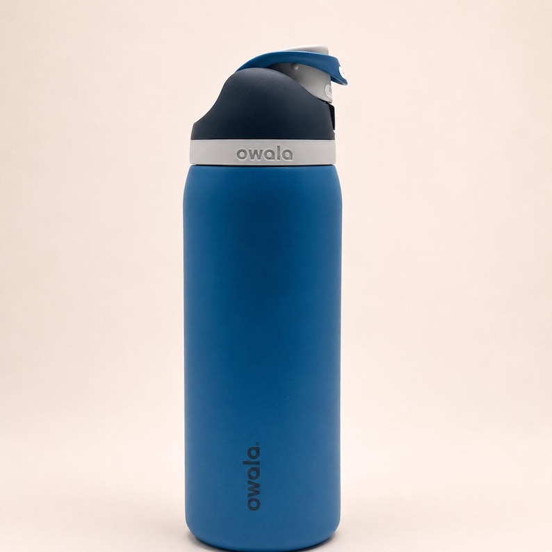 Pu&ograve; includere: Una borraccia blu Owala con un meccanismo di chiusura blu scuro e grigio chiaro. Il nome del marchio Owala &egrave; stampato in bianco sulla parte superiore grigia del coperchio e verticalmente in blu scuro sul corpo blu della borraccia.