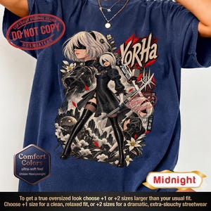Könnte beinhalten: Ein marineblaues T-Shirt mit einem Grafikdruck der Figur 2B aus Nier: Automata. Das Design zeigt die Figur in einem schwarzen Kleid mit einem Schwert, weißen Blumen und dem Text YorHa. Das T-Shirt hat einen Rundhalsausschnitt und kurze Ärmel.