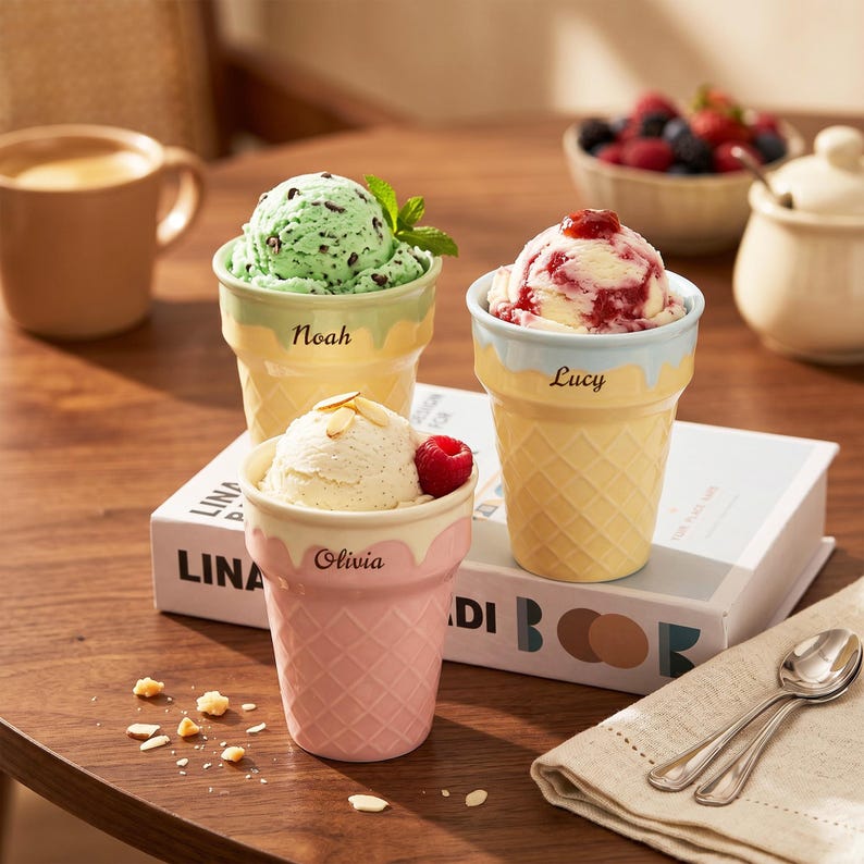 May include: Three ice cream bowls shaped like waffle cones, each with a different flavor of ice cream. One bowl has mint chocolate chip ice cream, one has vanilla with a raspberry, and one has a red berry swirl. Each bowl has a name on it.