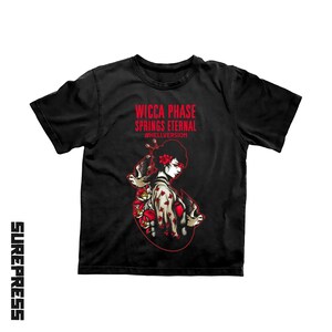 May include: A black short-sleeve t-shirt featuring a graphic of a person in a kimono surrounded by red flowers and birds. The text WICCA PHASE SPRINGS ETERNAL and #HELLVERSION are printed in red above the illustration. The word SUREPRESS is vertical.