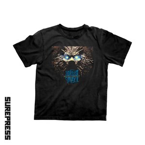 May include: A black short-sleeve t-shirt featuring a graphic print of a stylized creature with glowing blue eyes and intricate brown patterns. Below the creature, the text reads "MISS MAY I" and "MONUMENT" in a blue circular emblem design.