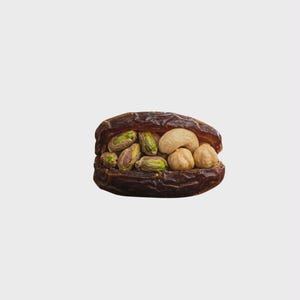 Puede incluir: Primer plano de un dátil grande, marrón oscuro, abierto y relleno de frutos secos. Los frutos secos incluyen pistachos verdes, anacardos tostados y avellanas redondas. El fondo es gris claro liso.