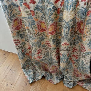 May include: A floor-length curtain featuring a repeating botanical pattern with large red and yellow flowers, blue-green acanthus leaves, and intricate scrolling vines on a light beige background, hanging in soft vertical folds.