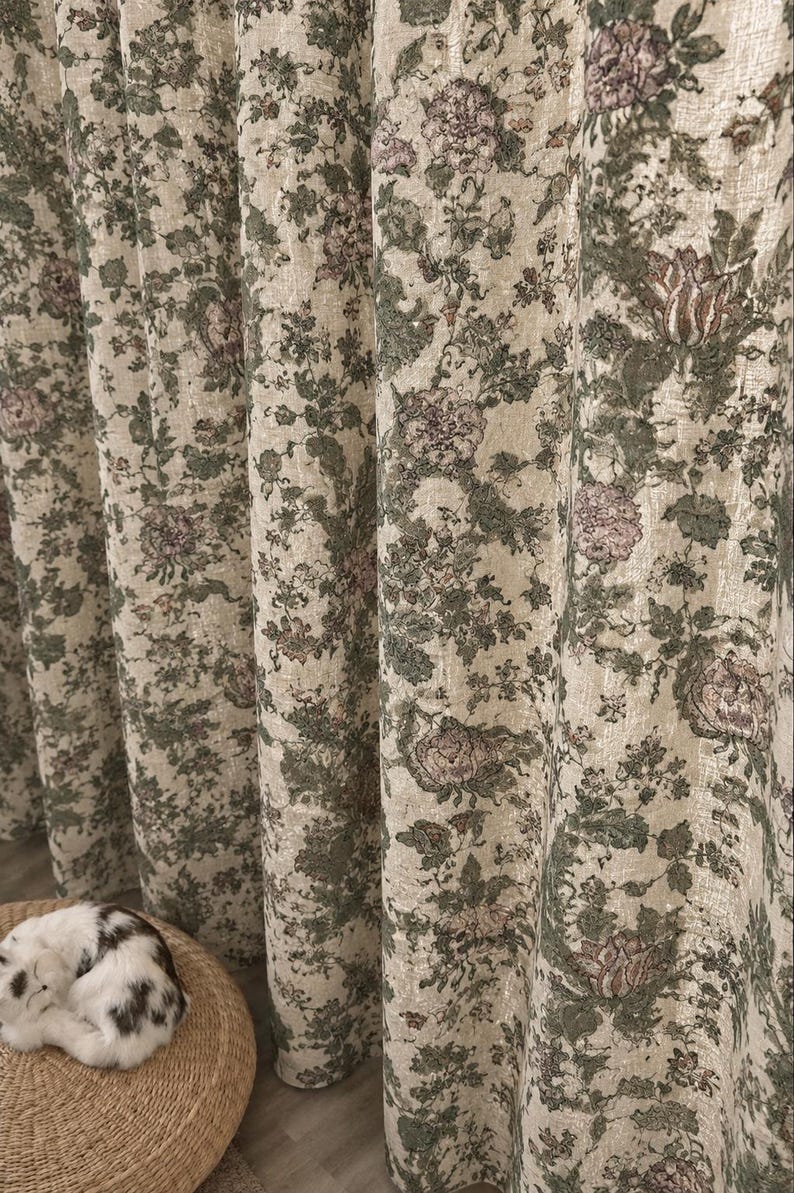 May include: Floor-length curtains featuring a cream-colored base fabric with an intricate floral pattern in shades of sage green and muted pink. The fabric has a textured, woven appearance with vertical folds creating deep, rhythmic pleats.