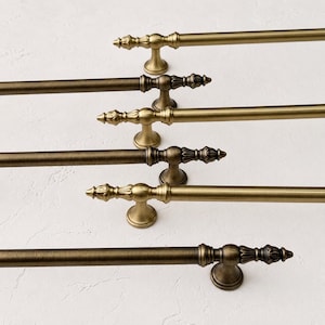 May include: A collection of five horizontal metal rods with a brushed antique brass finish. Each rod features a decorative finial with a pointed, fluted design and a matching circular mounting bracket positioned near the end of the rod.