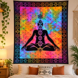 Könnte beinhalten: Ein rechteckiger Wandteppich mit der schwarzen Silhouette einer Person in sitzender Meditationshaltung. Die Figur zeigt sieben vertikal ausgerichtete Chakrasymbole vor einem lebendigen, mehrfarbigen Batik-Hintergrund mit kleinen schwarzen Sternen.