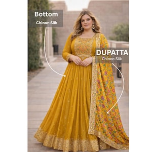 May include: A mustard yellow floor-length gown made of Chinon silk, featuring long sleeves, a round neckline, and intricate embroidery on the bodice. The skirt has a wide hem with gold embellishments. A matching floral dupatta is included.