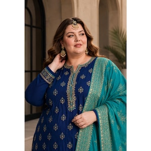 May include: A dark blue long-sleeved tunic featuring a gold embroidered pattern, a split neckline, and matching cuffs. A teal shawl with a gold floral print is draped over one shoulder. The ensemble is paired with gold dangling earrings and a maang tikka.