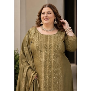 May include: An olive green salwar kameez with a gold floral design. The long-sleeved tunic has a round neckline and is worn with a matching scarf. The outfit is accessorized with silver jewellery and bracelets.