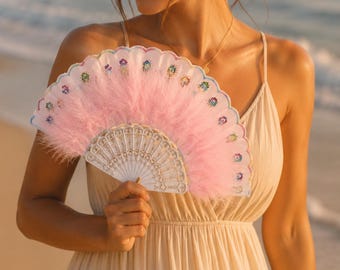 May include: A decorative hand fan with a white, intricately designed base and a fluffy pink feather section. The fan is adorned with colorful floral accents along the edge, creating a delicate and elegant accessory.