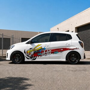 Puede incluir: Coche blanco con portón trasero y llantas negras. El coche tiene un gráfico de una calavera con una cinta amarilla y un diseño rojo y azul. El gráfico está en el lateral del coche. El coche está aparcado sobre una superficie pavimentada.